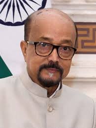 A headshot of Governor Ramen Deka, a man with glasses and a beard, in a formal light-colored Indian attire.